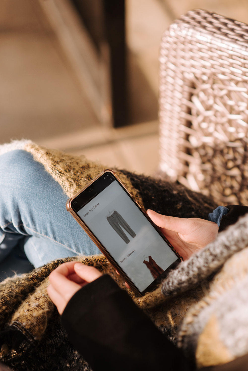 Close-up of an iPhone in a woman's hand as she scrolls through pants in an eCommerce store.